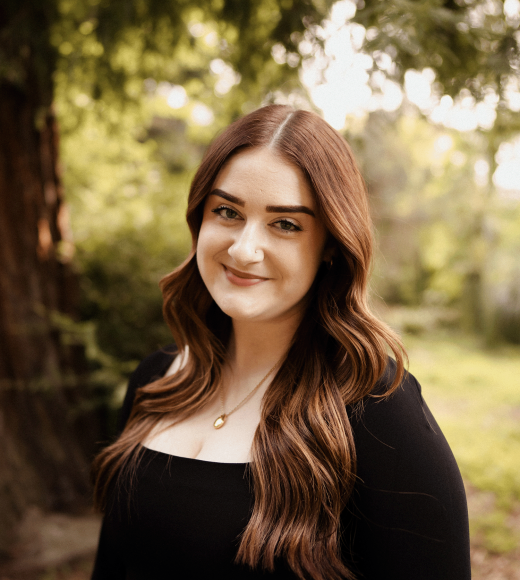 A photo of a woman with brown hair, and a tree in the background.