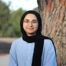 A woman wearing a head scarf and glasses near a tree.