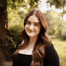 A photo of a woman with brown hair, and a tree in the background.